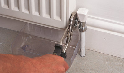 Using water pump pliers to loosen the nut that connects the radiator valve to the radiator.