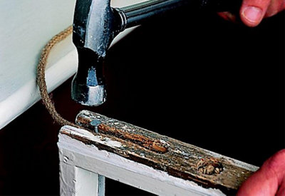 Using a hammer to tap a galvanised nail into the cord of a sash window to secure it in place.
