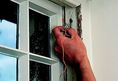 A person placing a cord with a nail tied around it into the hole above the pulley of a sash window.