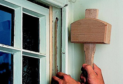 A person using a wooden mallet to tap the staff beads of a sash window into place.