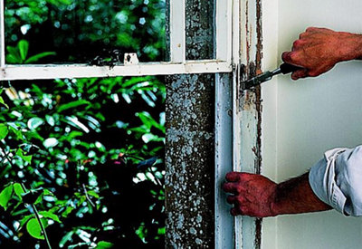 A person using a chisel to prise the narrow parting beads on a sash window out of their grooves.