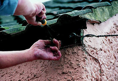 Person securing a gutter bracket to a fascia board using a screwdriver.
