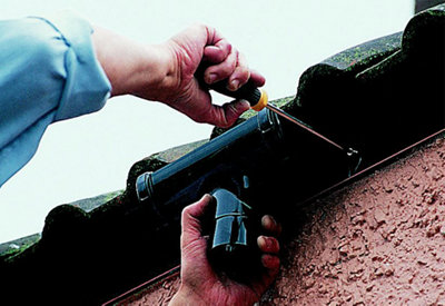 Person using a screwdriver to secure a gutter outlet to a fascia board.