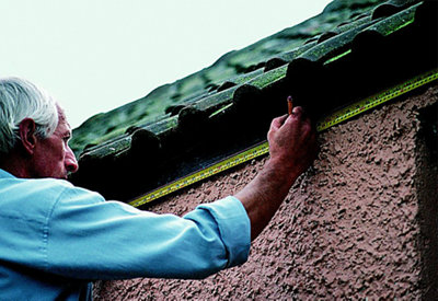 Person using a pencil to mark the position of gutter brackets on a fascia board. Tape measure sits underneath the fascia board to show where brackets should be installed.