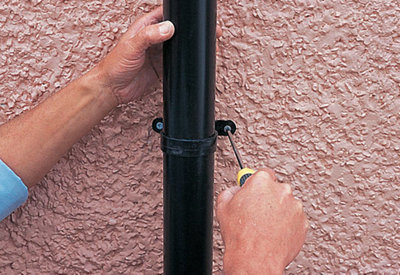 Person using a screwdriver to secure a gutter pipe clip to a wall.