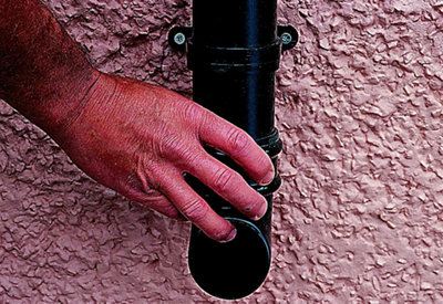 Person securing an angled gutter shoe to the bottom of a gutter downpipe.