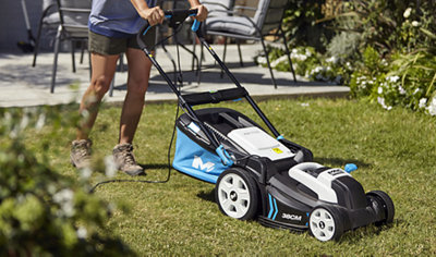 Person using a corded lawnmower to cut the grass in a small garden.