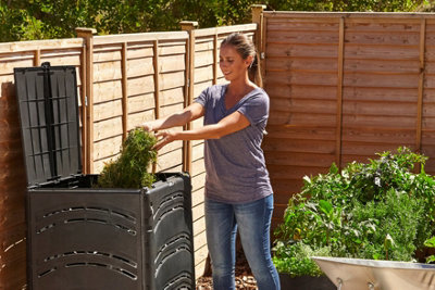 Person adding freshly cut grass clippings into an open compost bin in a garden.