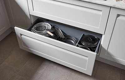A light grey deep kitchen drawer is open to reveal various cooking pots and pans. The drawer has dividers for easier storage, and the drawer front has an integrated handle.