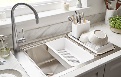 A chrome sink with mixer tap is nestled within a white and grey marble-effect countertop. The sink features a white drainage caddy and bowls and cutlery are placed to the side.