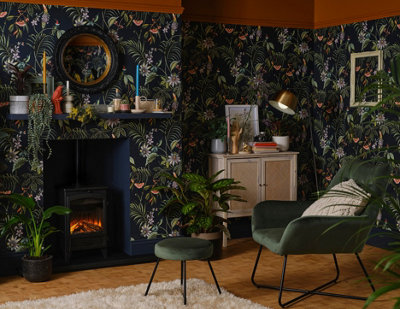 A living room with jungle print wallpaper, a green armchair and footstool and plenty of houseplants.