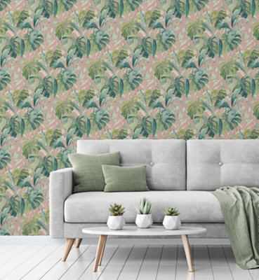 Jungle leaf green and pink wallpaper in a living room with a grey sofa and green cushions.