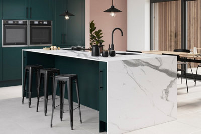 A large marble kitchen island in a pink and green kitchen with white flooring.