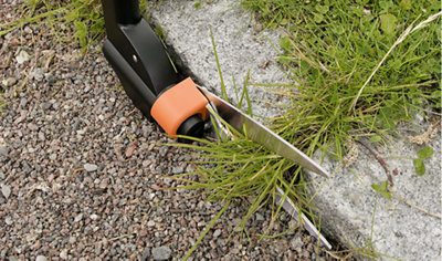A pair of edging shears trimming grass which has grown on top of a paving slab.