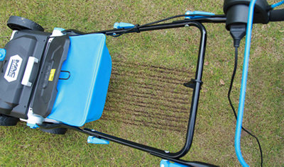 Top down view of a scarifier running across a lawn. The scarifier has left grooves in the section of lawn it has just passed across.
