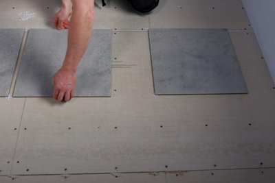 Person laying floor tiles on top of tile backer board without any adhesive to plan the layout.