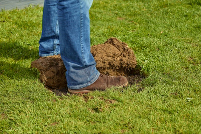 Person using using their foot to level the soil where a section of turf has been pulled back.