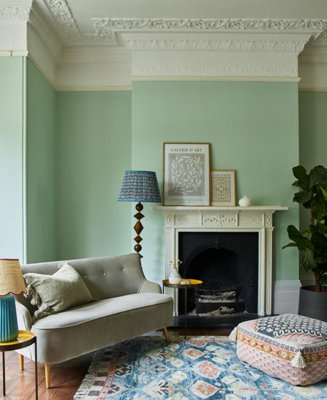 A grand living room with intricate coving, pistachio green walls, and a mantelpiece painted to match the ceiling.
