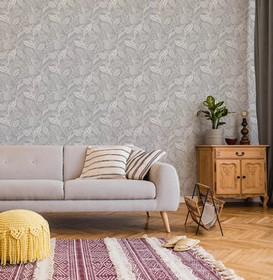 Light grey living room with leaf patterned wallpaper, grey sofa with striped cushions, a yellow footstool, and a red and white geometric tasseled rug.