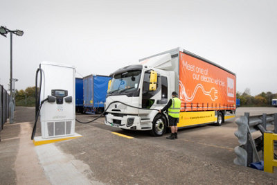 Man charging a B&Q electric van at pod point charging point in a car park.