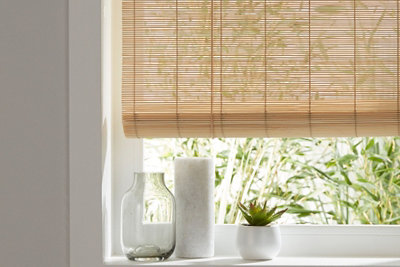 A bamboo roller blind attached to a window in a white room.