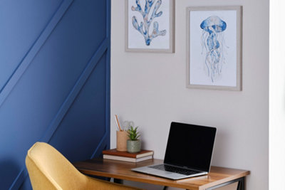A white and blue home office with a wooden desk, yellow upholstered desk chair and two framed art prints on the wall.