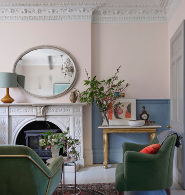 An ornate living room with detailed coving and fireplace and green armchairs.