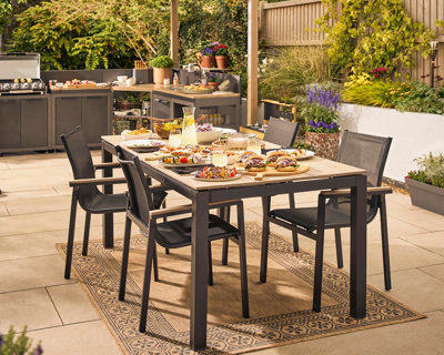 BBQ food on a GoodHome Aconite Metal 6 seater Rectangular Dining table with rug beneath.