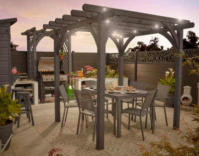 Grey pergola sheltering a garden dining table set, with an outdoor kitchen in the background.