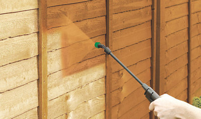 A person using a paint sprayer to apply an even coat of paint to a garden fence, ensuring a smooth and consistent finish.