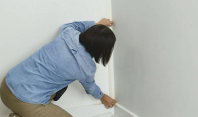 Person applying a piece of masking tape to the corner where two walls meet.