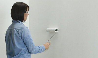 Person wearing safety glasses running a paint roller vertically across a wall.