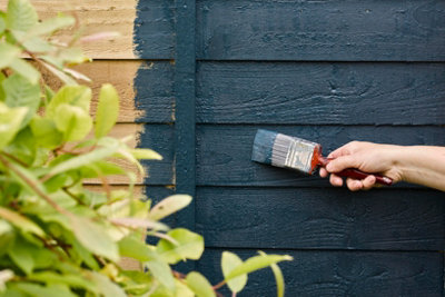 A person using a paint brush to paint their fence blue.