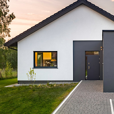 The exterior of a modern bungalow painted in a fresh white, with the front door and surrounding area painted in a contrasting dark grey. Shop GoodHome masonry paint.