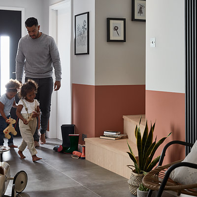 Family in their stylish hallway painted a terracotta on the bottom half of the walls and white on the top. Shop GoodHome durable paint.