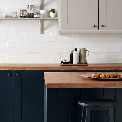 Dark blue kitchen cupboard with dark wood countertops and white metro splashback tiles. Shop GoodHome metal and wood paint.