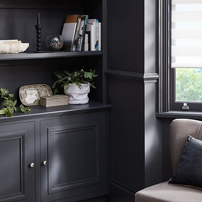 A cosy sitting area with built in shelves and cabinet painted in a very dark blue and decorated with vases and books. Shop GoodHome metal and wood paint.
