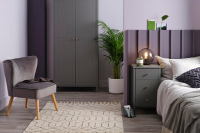 Purple bedroom with dark grey wardrobe and bedside table, and a purple velvet statement chair.