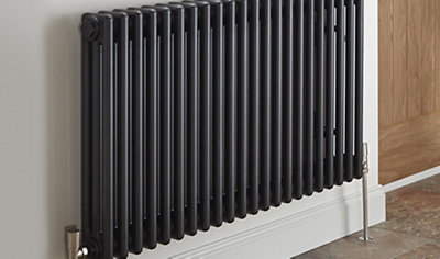 Small black column radiator mounted on white wall with chrome valves.