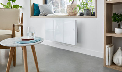 White flat panel radiator with flat front divided into 3 sections. Radiator is hung on white wall inside room with grey floor and modern wood furniture.