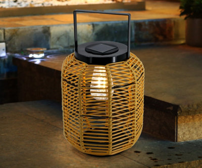 A small garden lantern with a bulb inside a rattan-style shade, featuring a handle and a solar panel on the top.