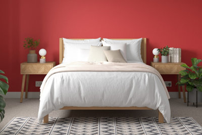 Bedroom with light wooden bed and bedside tables, white bedding, a white and grey geometric print rug and, bright red painted walls.