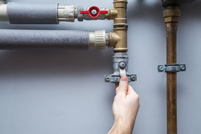 Person turning a valve between two sections of pipe to switch off a water supply.