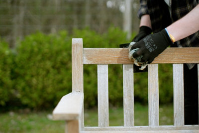 A person wearing gloves treating a wooden garden bench.