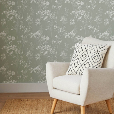 Sage green and white floral wallpaper in a living room with a cream upholstered armchair.