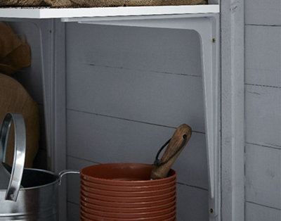 A white heavy-duty metal bracket installed in a shed, with tools and a watering can below.