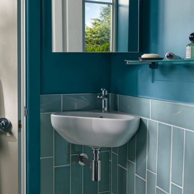 Small white basin in corner of blue bathroom with a floating shelf placed next to it.