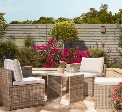 A small paved garden with an outdoor coffee set, and a large border behind with a tall tree that acts as a focal point.
