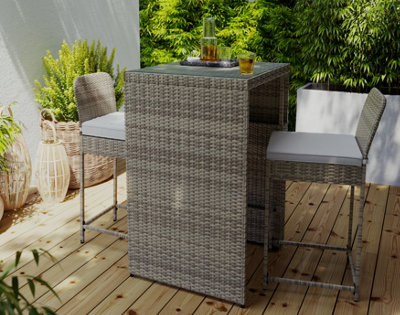 A grey garden bar table with bar stools on a wooden deck in a garden.
