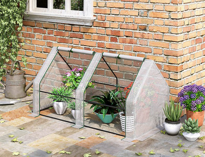 A small greenhouse full of small potted plants, placed besides an exterior brick wall.